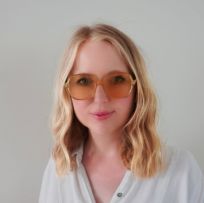 A headshot photo of musician Polly Scattergood, a smiling woman with large glasses blonde hair